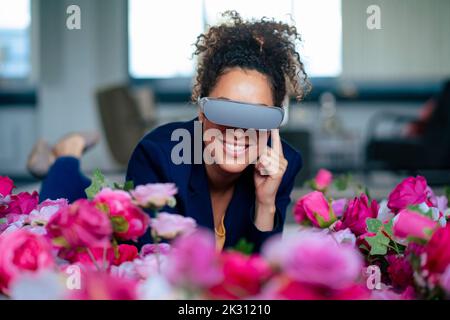 Smiling businesswoman using VR glasses by flowers at office Stock Photo