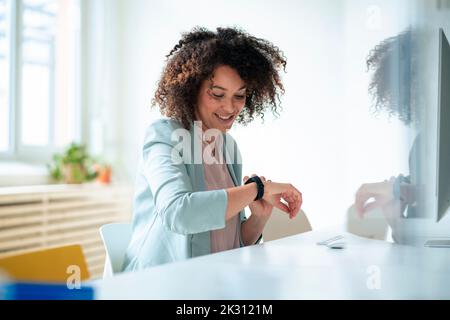 Smiling businesswoman with curly hair checking time on smart watch at office