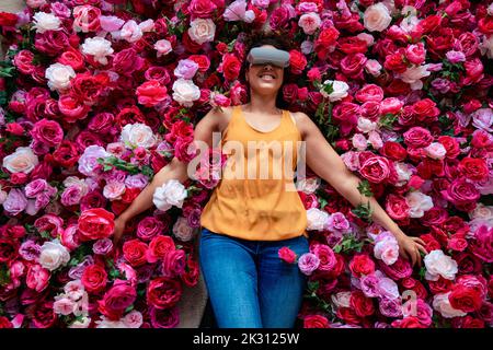 Mature woman wearing VR glasses lying on flowers Stock Photo