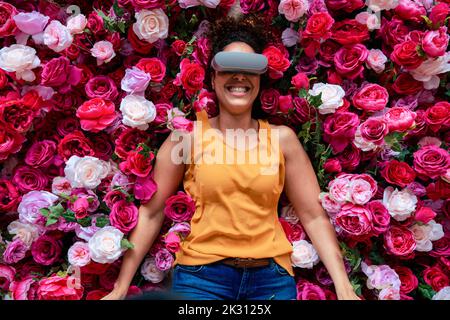 Cheerful woman wearing VR glasses lying on flowers Stock Photo