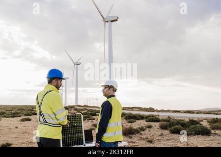 Engineers discussing with each other by wind turbines at wind farm Stock Photo