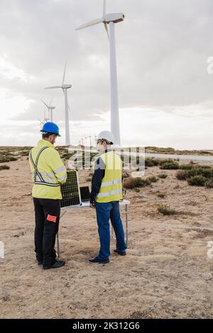 Engineers talking to each other standing at wind farm Stock Photo