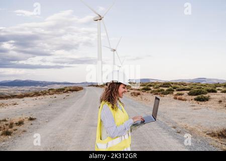 Smiling engineer working on laptop at wind farm Stock Photo