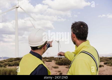 Engineers discussing over wind turbine model at wind farm Stock Photo