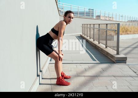 Exhausted woman taking break from exercise leaning on wall Stock Photo