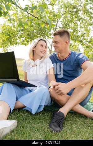 Young woman sitting with laptop holding hand of boyfriend at park Stock Photo