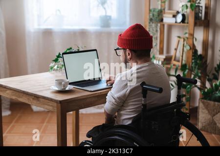 Man in wheelchair using laptop at home Stock Photo