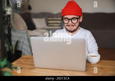 Smiling man wearing knit hat using laptop at home Stock Photo