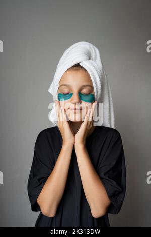 Girl with towel wrapped on head standing against gray background Stock Photo