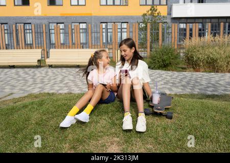 Happy girls with smart phones sitting on grass Stock Photo