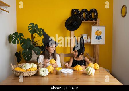 Smiling sisters painting pumpkin on table at home Stock Photo