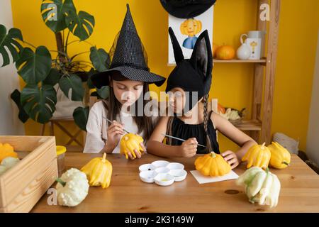 Girl with sister painting pumpkin on table at home Stock Photo