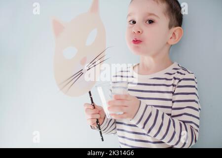 Boy drinking glass of milk and holding mask by wall Stock Photo