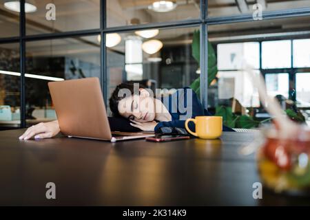 Tired businesswoman with laptop taking nap in office Stock Photo