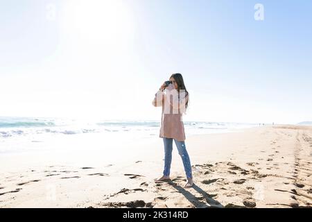 Girl standing with camera taking photos at beach