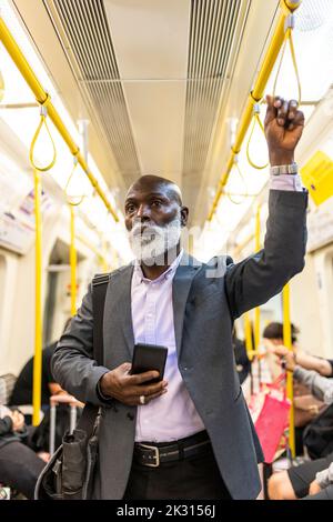 Senior commuter with mobile phone holding handle in train Stock Photo