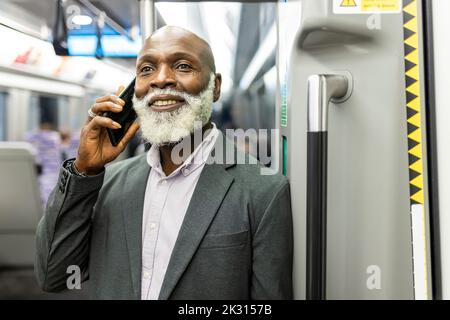 Smiling businessman talking on smart phone in train Stock Photo