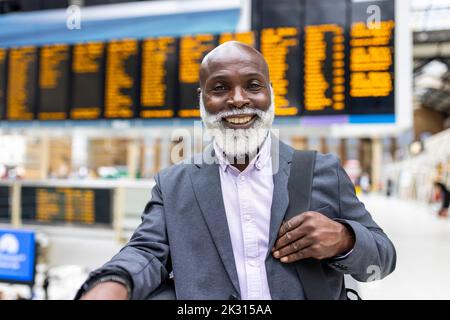 Smiling senior businessman carrying laptop bag at station Stock Photo
