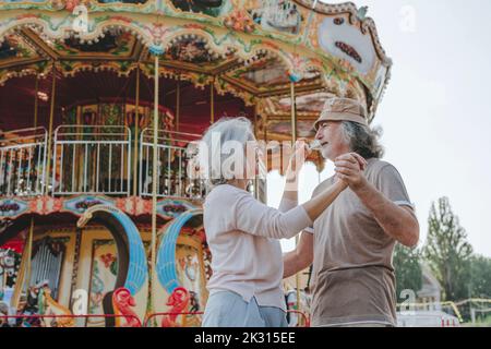 Smiling couple dancing together in front of carousel Stock Photo