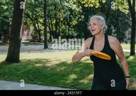 Mature woman having fun playing frisbee in park Stock Photo
