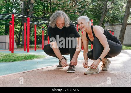 Happy couple tying shoelaces in park Stock Photo