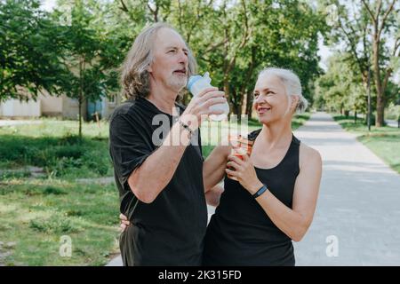 Mature woman with senior man drinking water in park Stock Photo