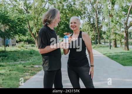 Woman and senior man drinking water in park Stock Photo