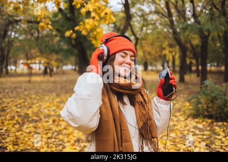 Happy young woman holding mobile phone enjoying music through headphones at park Stock Photo