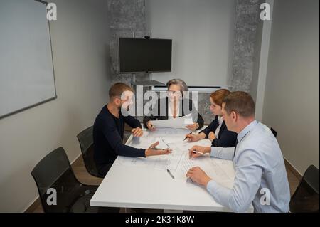 Four colleagues are discussing blueprints in a conference room in an office. Brainstorming of engineers and architects. Stock Photo