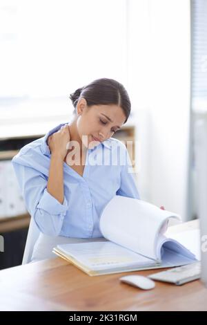 My poor neck muscles...a beautiful young woman working at her desk in the office. Stock Photo