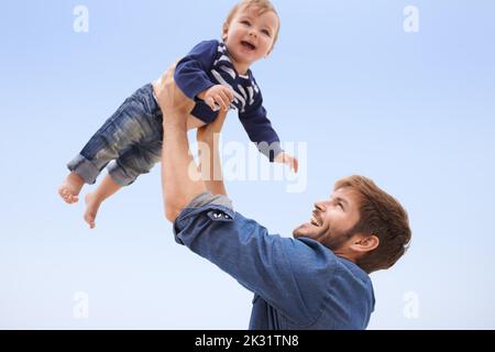 He only has eyes for his boy. a young man lifting his son up into the air. Stock Photo