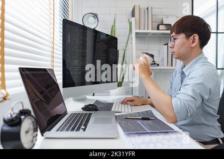 Software development concept, Male programmer checking website programming and drinking coffee. Stock Photo
