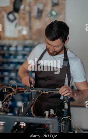 Smiling young worker repairing coffee machine in a workshop Stock Photo