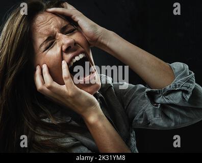Someone please help. A young woman screaming uncontrollably while isolated on a black background. Stock Photo