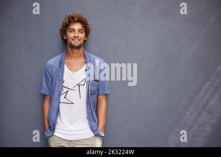 Cool and casual. A handsome young man leaning against a bluegray wall. Stock Photo