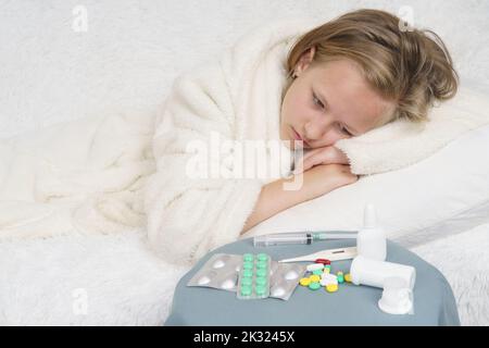 A sick teenage girl lies on the bed and looks at the medicine. Medical concept. Stock Photo