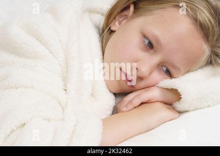 Sick teenage girl lies on the bed and looks away. Medical concept. Stock Photo