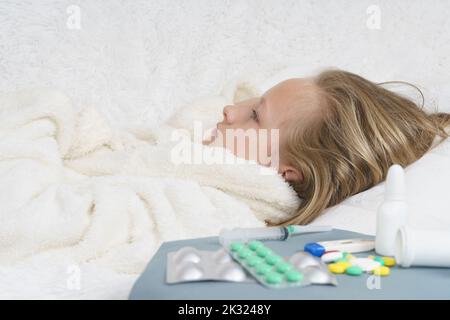 Sick teenage girl lies on the bed next to lying medication. Medical concept. Stock Photo