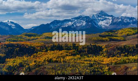 An amazing shot of the snow-capped mountains with yellow- leaved trees in the foreground during autumn Stock Photo