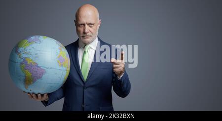 Confident corporate businessman holding a globe and pointing, blank copy space Stock Photo