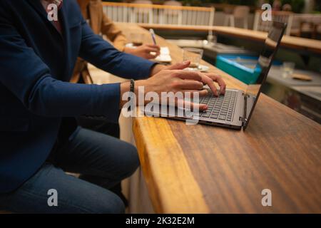 A young businessman is working on his lap top, indoors, at a cafeteria's terrace Stock Photo