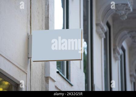 A white horizontal sign board with blank white sign mock up hangs on the wall of an old classic building Stock Photo