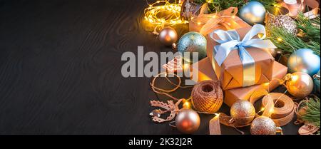Gift boxes with blue ribbons and Christmas tree toys on a black background with a burning garland. Stock Photo