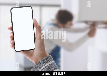 Woman holding a smartphone and plumber fixing a boiler in the background, home repair service concept Stock Photo