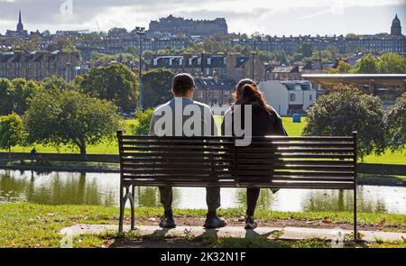 Inverleith park, Edinburgh Scotland, UK. 24th September 2022. Morning sunshine after a cloudy start to the day, temperature mid morning around 9 degrees rising to 13 degrees by lunchtime. Pictured this couple relax on a park bench with Inverleith pond and Stockbridge mid ground and the architecture of the city in the background. Credit: Arch White/alamy live news. Stock Photo