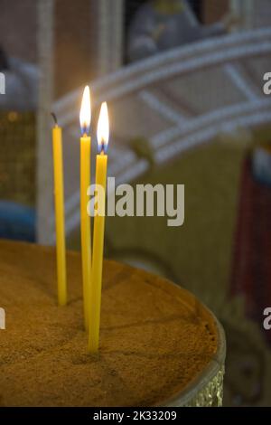 Burning candles in church. Religious concept. Many burning candles shining against backdrop of painted wall. Shallow depth of field. Stock Photo