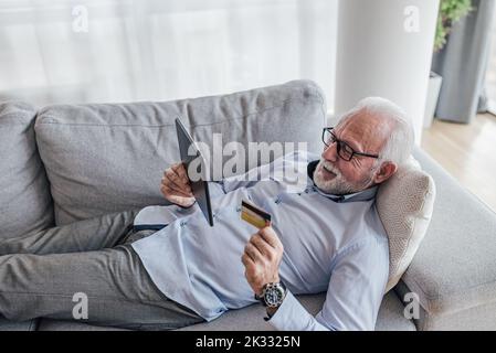 Calm old man, checking his credit card number and using his tablet to order something online. Stock Photo