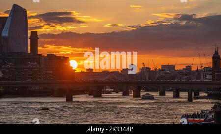 London Bridge Sunset: Sunset over London Bridge, with an orange sky, silhouetted buildings and river taxis on the Thames. Shot from Tower Bridge. Stock Photo