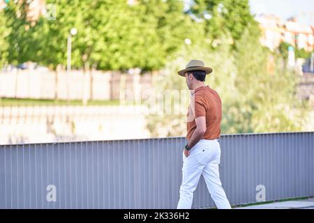 Stylish man wearing a hat and using his mobile phone while walking outdoors in a park. Technology concept. Stock Photo