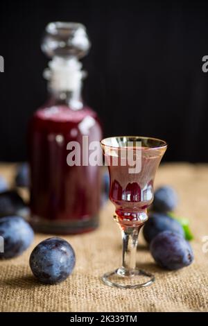 plum red wine in a glass and a decanter against the background of ripe large plums on the table. Stock Photo